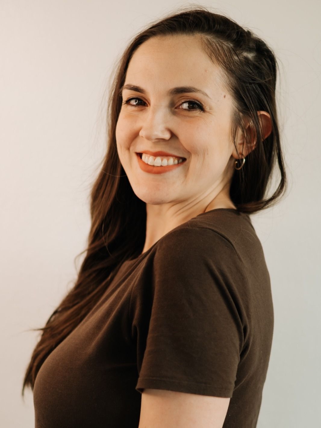 Camila Magnusson, smiling, in a brown t-shirt against a pale wall