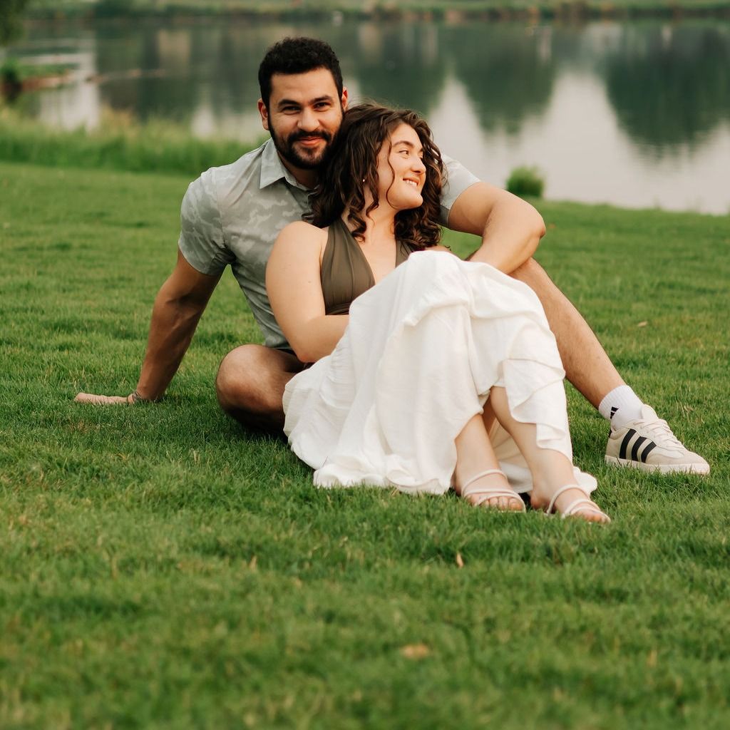 A couple sitting on the lawn by a pond
