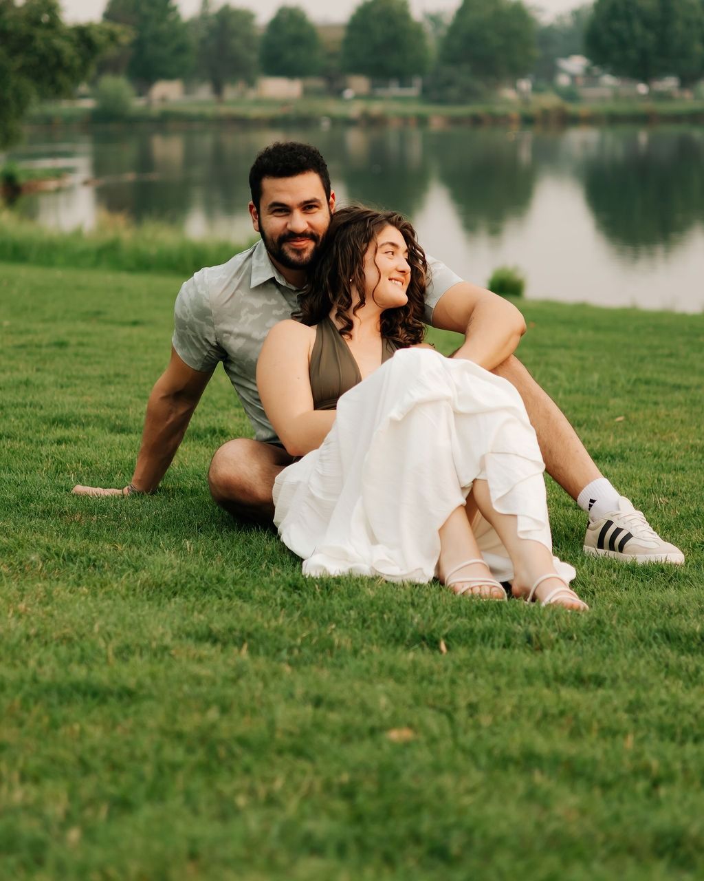 A couple sitting on the lawn by a pond