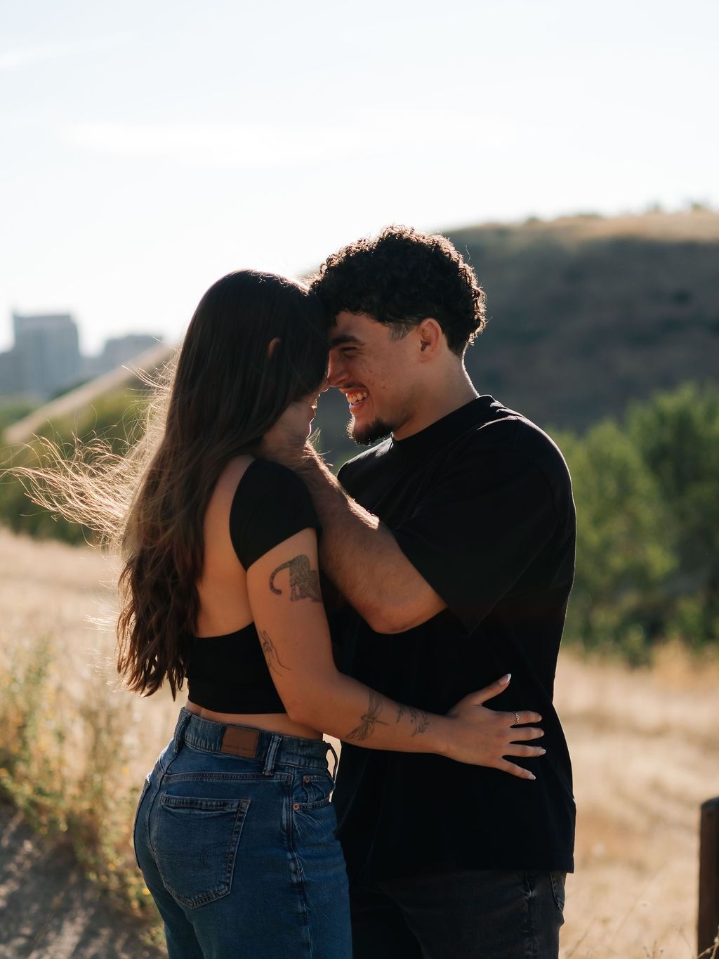 A couple embracing on a foothill of dry grass as the sun sets behind them