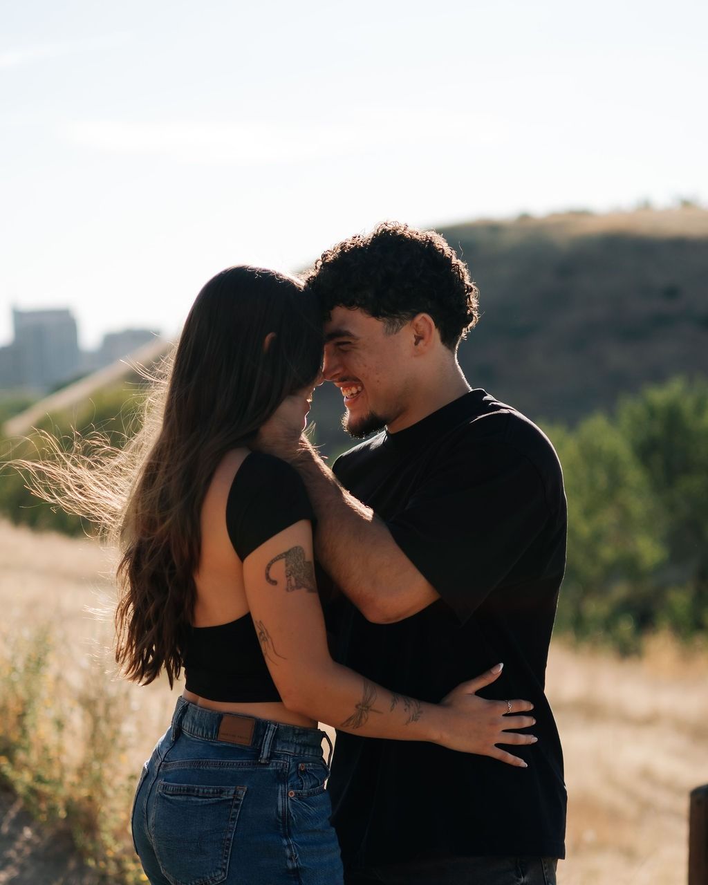 A couple embracing on a foothill of dry grass as the sun sets behind them